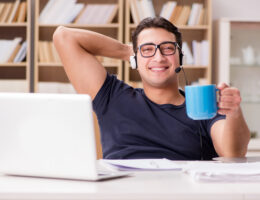 man sitting at his computer working from home with a blue mug of coffee in his hand