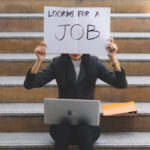 woman working on her laptop is holding up a sign that says looking for a job