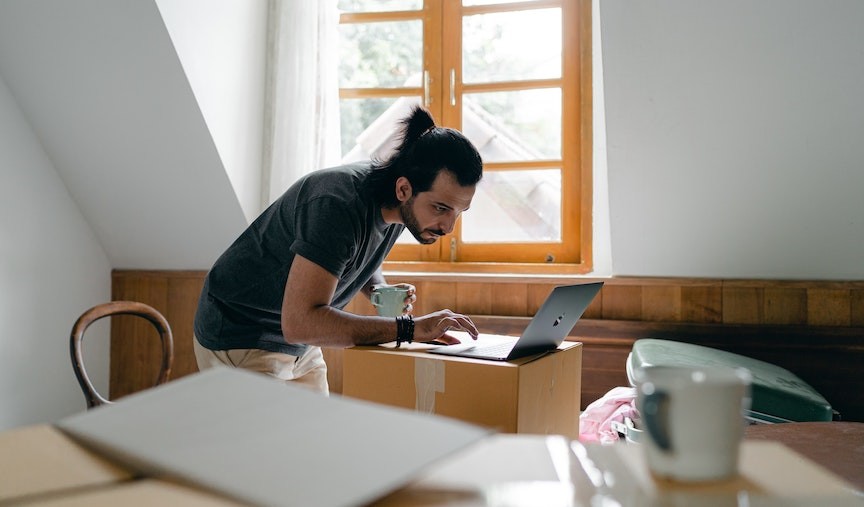 man on computer looking for a job in a new city while packing up his home